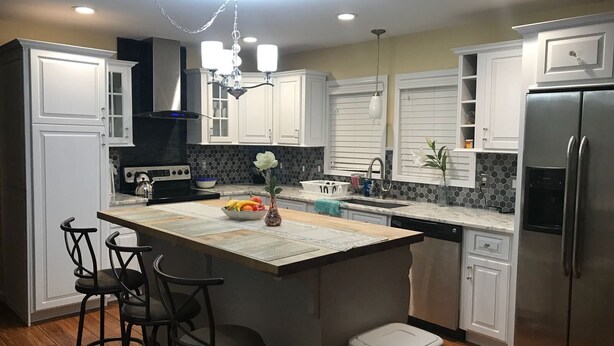 A modern kitchen with white cabinetry, a central island with bar stools, a stainless steel refrigerator, and a chandelier. - 6BR Family Retreat - Heated Pool & Game Room - Near Lake George & Saratoga (Corinth)