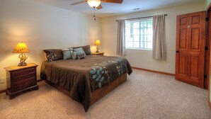 Een slaapkamer met een bed, twee nachtkastjes met lampen, een plafondventilator, een raam met gordijnen, en een houten deur.