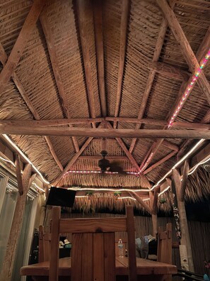 Une structure à toit de chaume, avec des poutres en bois et un ventilateur de plafond.