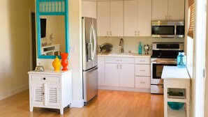 Une cuisine moderne avec des meubles blancs, un réfrigérateur en acier inoxydable, un four à micro-ondes et un évier. Un poisson décoratif est accroché au mur, et il y a un miroir avec un cadre bleu.