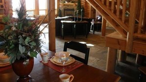 A dining area with a wooden staircase, a fireplace, and a view of the kitchen. - Luxurious Log Home with Mille Lacs Lake Sunrise Views (Garrison)
