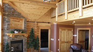 A spacious living room with a fireplace, wooden ceiling, and a cozy seating area. - Luxurious Log Home with Mille Lacs Lake Sunrise Views (Garrison)