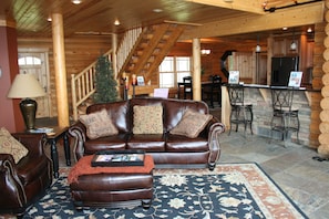 Cozy cabin interior with a central seating area, staircase, and kitchen.