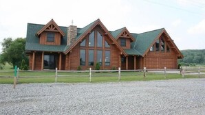 A log cabin with a green roof, large windows, and a stone chimney. - Luxurious Log Home with Mille Lacs Lake Sunrise Views (Garrison)