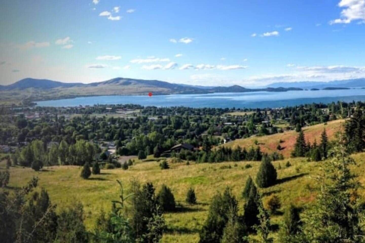 A panoramic view of a coastal town with a lake, hills, and a red balloon.