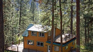 A multi-story yellow cabin with a balcony, surrounded by tall pine trees. - Peaceful, Private Cabin overlooking the Clearwater River. Dbl occ rates (Orofino)