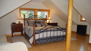 A bedroom with a sloped ceiling, a bed with a metal frame, two bedside tables with lamps, and a wooden floor. - Peaceful, Private Cabin overlooking the Clearwater River. Dbl occ rates (Orofino)