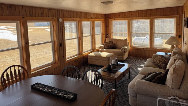 A cozy room with wooden walls, large windows, a sofa, a table, and chairs. - Shady Pines Retreat  (Ontario)