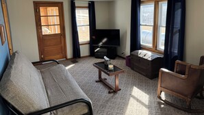A living room with a sofa, a chair, a small table with a candle, a television, and a window with curtains. - Shady Pines Retreat  (Ontario)