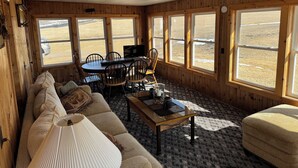 A cozy cabin interior with a wooden interior, a sofa, a dining table with chairs, and large windows offering a view of a snowy landscape. - Shady Pines Retreat  (Ontario)