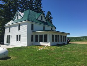 Situated on a grassy area, this two-story house features a spacious porch with multiple windows.