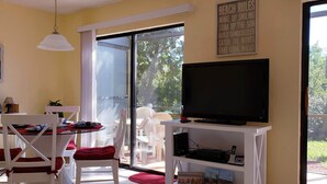 Une pièce comprenant une table à manger, des chaises, un téléviseur et une grande fenêtre.