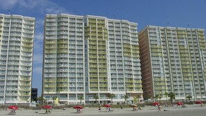 Ett högt hotell med flera balkonger, ett läge vid stranden och röda parasoller på bottenvåningen.