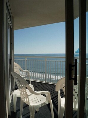 Un balcon avec des chaises en plastique blanches et une vue sur l’océan.