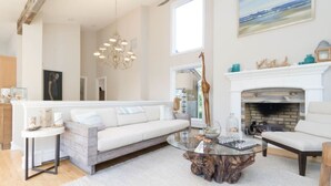 A spacious living room with a white sofa, a glass coffee table, and a fireplace.