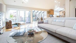 A spacious living room with a large sofa, a glass coffee table, and a view of the city through large windows.