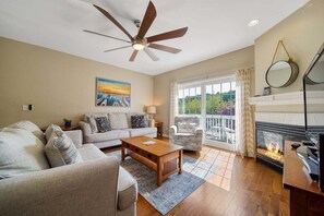 A living room with a ceiling fan, a fireplace, a sofa, a coffee table, and a view through the glass door.
