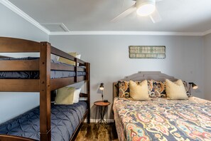 Une chambre avec un lit superposé, un lit simple, une petite table avec une lampe et un ventilateur de plafond.