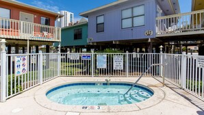 Un espace piscine avec un jacuzzi, entouré d’une clôture blanche, et bordé d’immeubles aux couleurs vives.