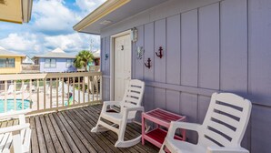 Un balcon avec deux fauteuils à bascule blancs et une petite table rose, donnant sur un espace piscine.