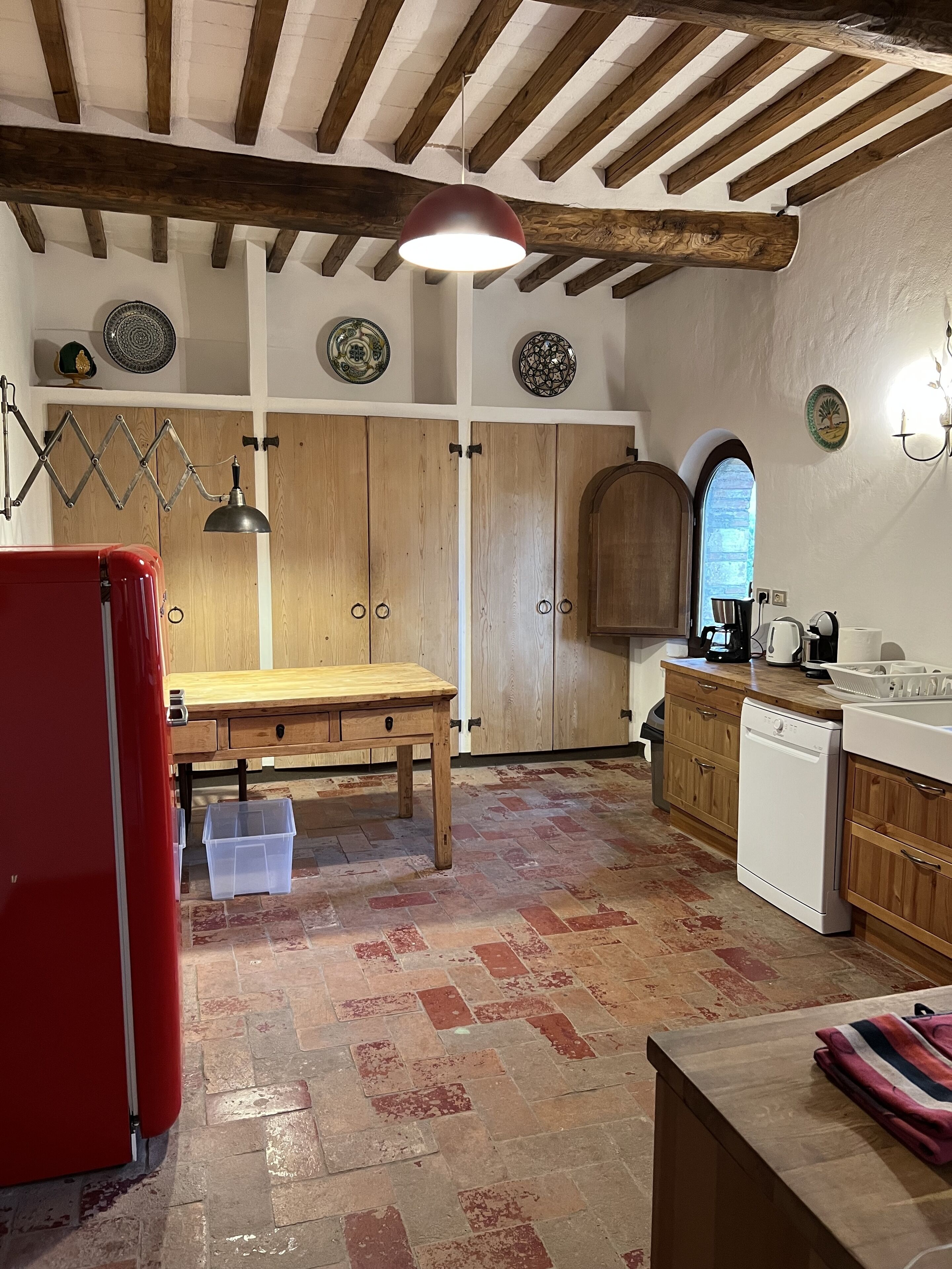 Une cuisine avec des meubles de rangement en bois, un réfrigérateur rouge, une table en bois et un lave-vaisselle.