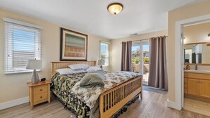 Een slaapkamer met een houten bed, nachtkastje, plafondlamp en uitzicht buiten door een schuifdeur.