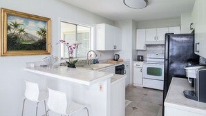 Une cuisine moderne avec des meubles blancs, un réfrigérateur noir, un évier et un petit îlot central avec des chaises.