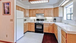 A kitchen with wooden cabinets, a white refrigerator, a black stove, and a window providing natural light. - Yosemite Pines (Yosemite)