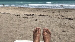 A beach scene with a person lying on a sunbed, facing the ocean.