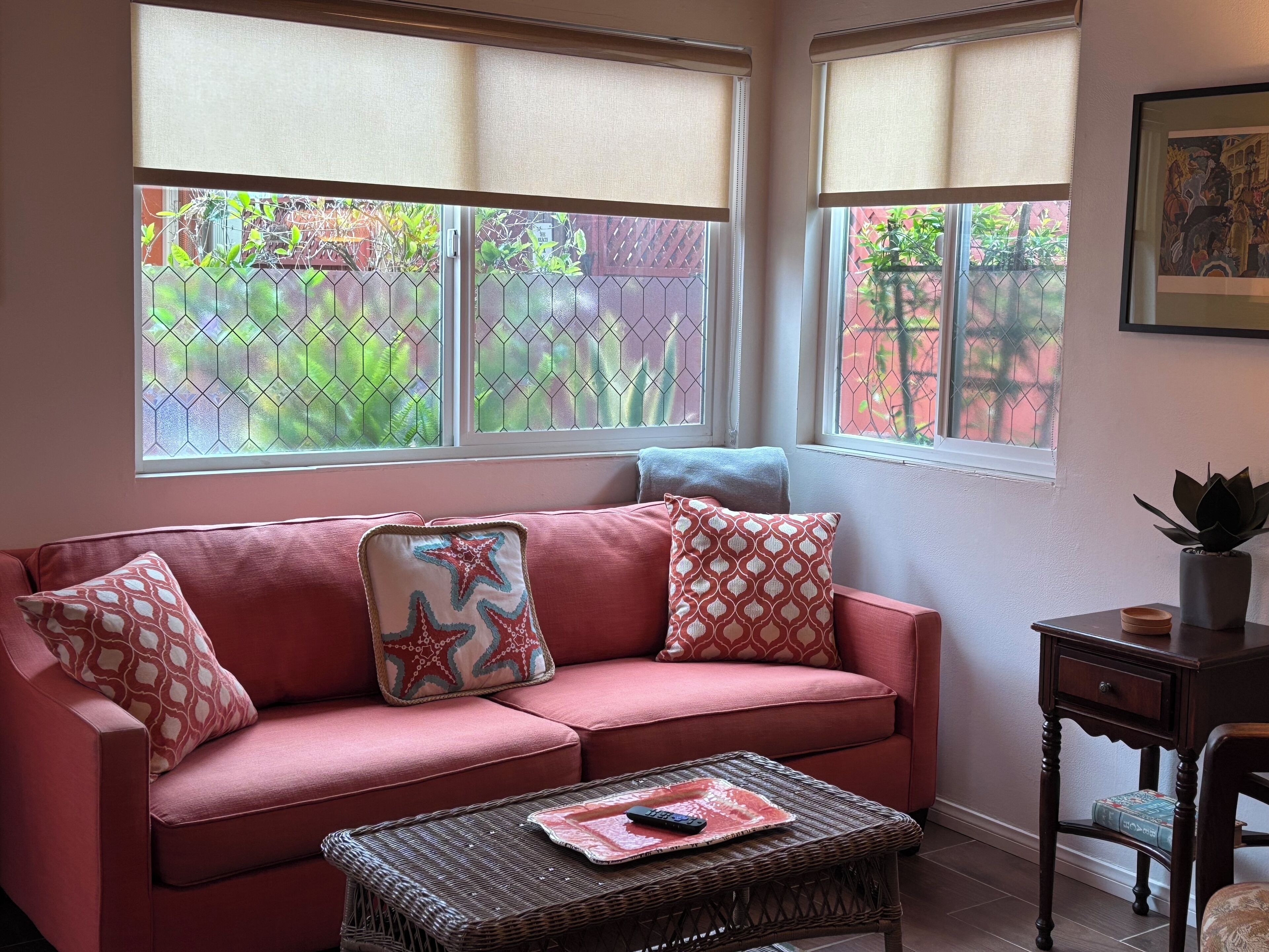 A room with a pink sofa, a wicker coffee table, and a small wooden side table.