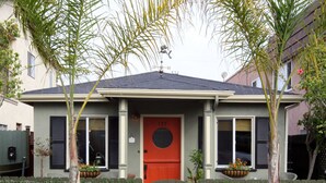 A two-story house with a red door, number 137, and a small front yard with potted plants and a star-shaped decoration.