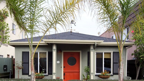 Une maison à deux étages avec une porte rouge, le numéro 137, et un petit jardin devant, agrémenté de plantes en pot et d’un décor en forme d’étoile.
