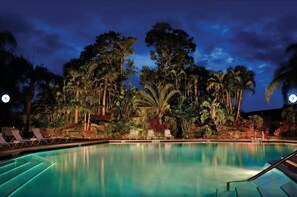 A nighttime pool area with lounge chairs and tropical vegetation. - Park Shore Resort Modern Top Floor 2 Bed, 2 Bath  (Naples)