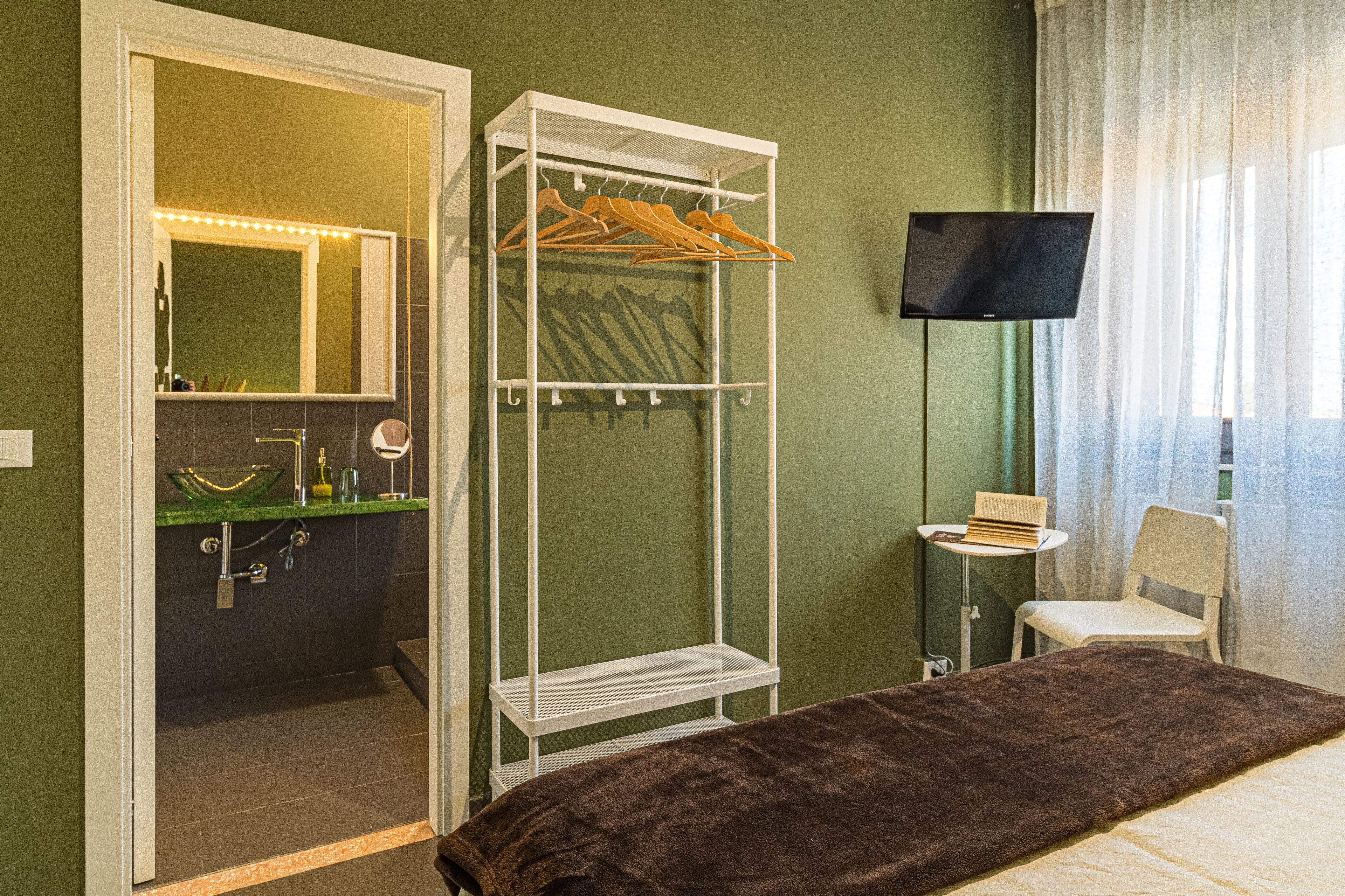 Ein Hotelzimmer mit Bett, begehbarem Kleiderschrank, Fernseher, Stuhl und kleinem Tisch.