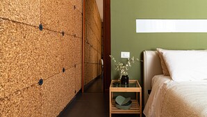 A hotel room with a textured wall, a small wooden side table with a vase of flowers, a bed with white bedding, and a green accent wall. - B&B Lotus House (Lanciano)