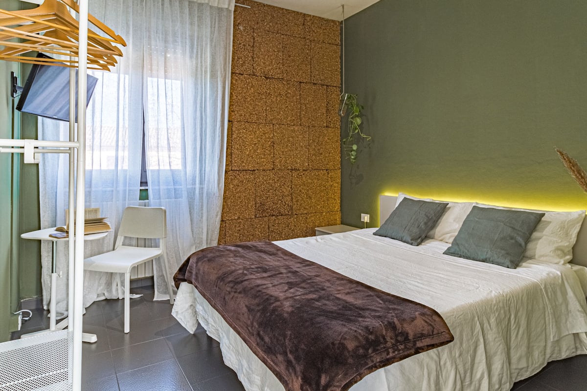 A modern bedroom with a large bed, a bedside table, a chair, and a hanging clothes rack.