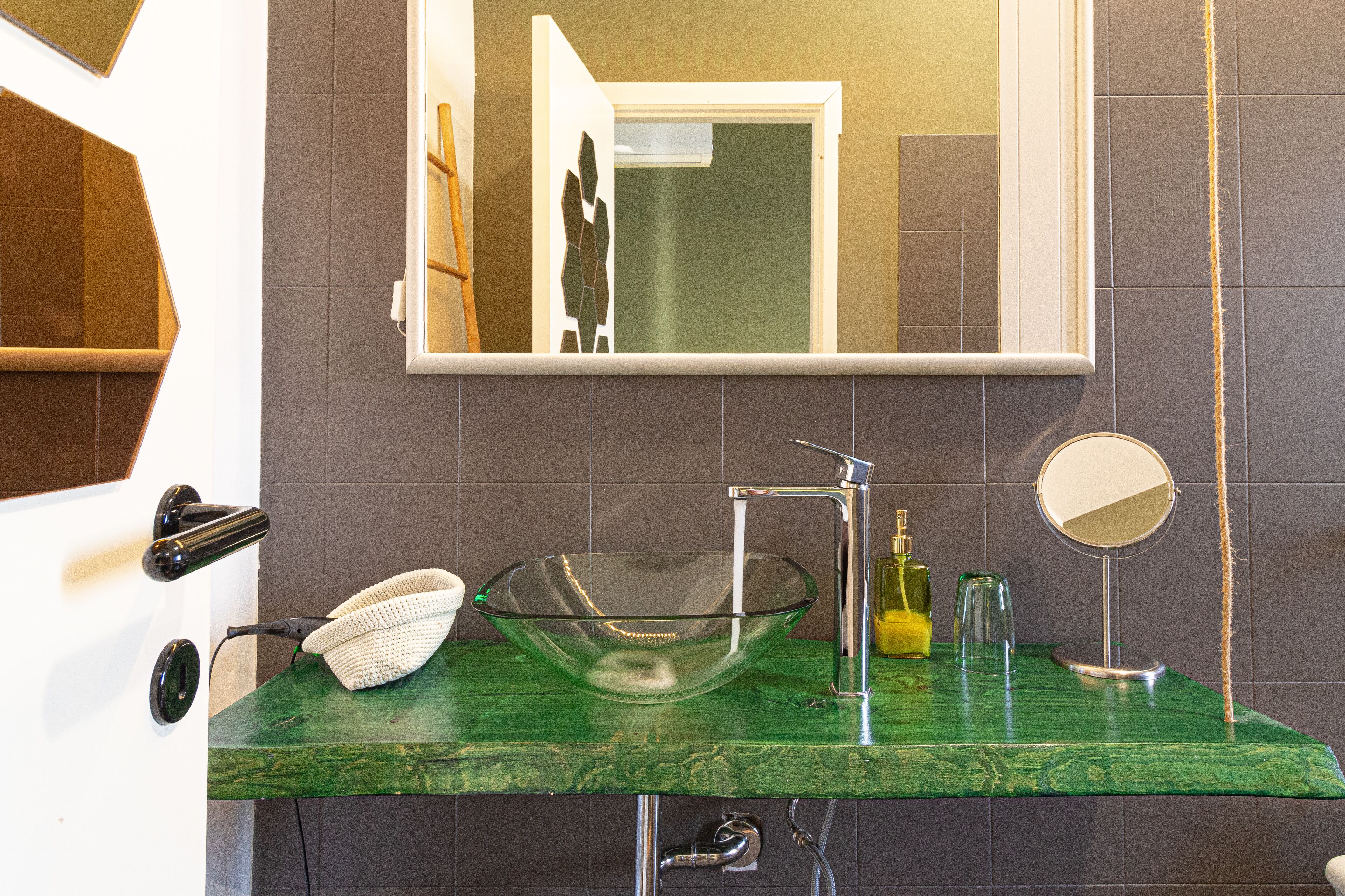 A bathroom with a green marble sink, a glass bowl sink, a mirror, and a towel rack.