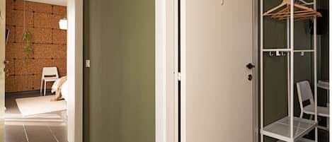 A hallway with a white door, a metal shelving unit with hangers, and a chair.