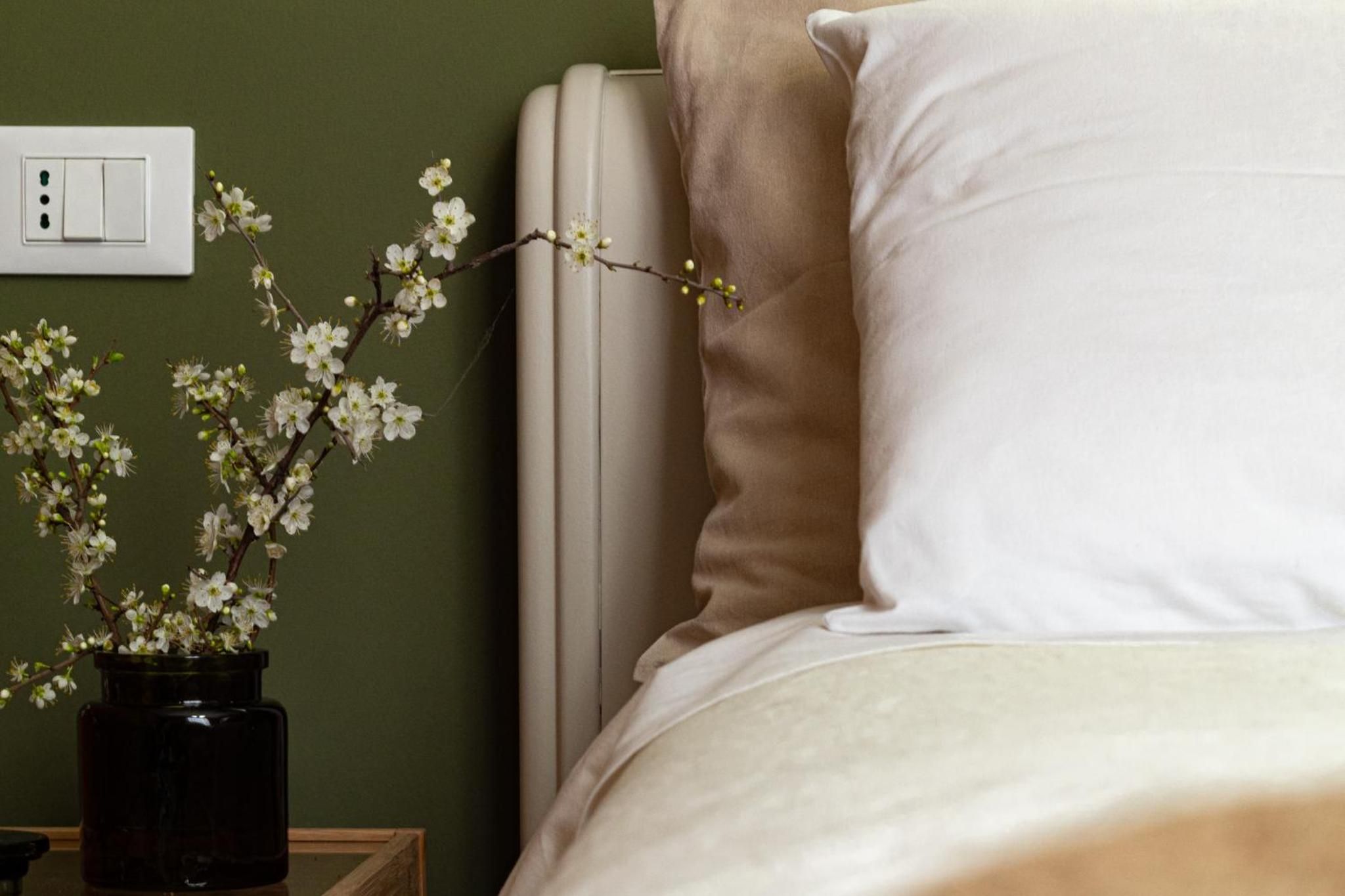 Un dormitorio con una cama, una mesita de noche con un jarrón de flores y un enchufe de pared.