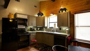 Une cuisine avec des meubles de rangement en bois, un réfrigérateur noir, une cuisinière et un tabouret rouge.