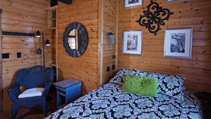 Une pièce de style cabane en bois, avec un lit, une chaise, une petite table et un miroir au mur.