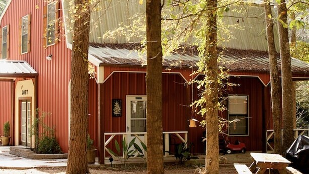 Un bâtiment rustique de couleur rouge, doté d’un porche et entouré d’arbres.