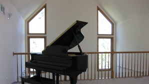 Un pianoforte a coda in un'ampia stanza con grandi finestre e una ringhiera in legno.