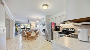 A modern kitchen with white cabinetry, a stainless steel refrigerator, a built-in oven, and a sink. There is a dining area with a table and chairs. - Hilton Head Tennis Villa  (Hilton Head Island)