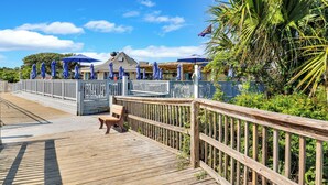 A wooden boardwalk with a bench, blue umbrellas, and a building with a sloped roof. - Hilton Head Tennis Villa  (Hilton Head Island)
