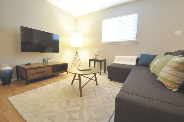A living room with a flat-screen TV, a lamp, a sofa, a coffee table, and a small side table.