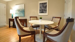 Un área de comedor con una mesa redonda, cuatro sillas, una pequeña planta en maceta y dos cuadros en la pared.