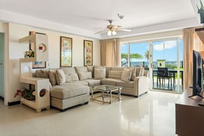 A living room with a sectional sofa, a glass coffee table, and a ceiling fan.