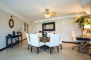 A dining area with a round table, white chairs, a ceiling fan, and a decorative mirror.