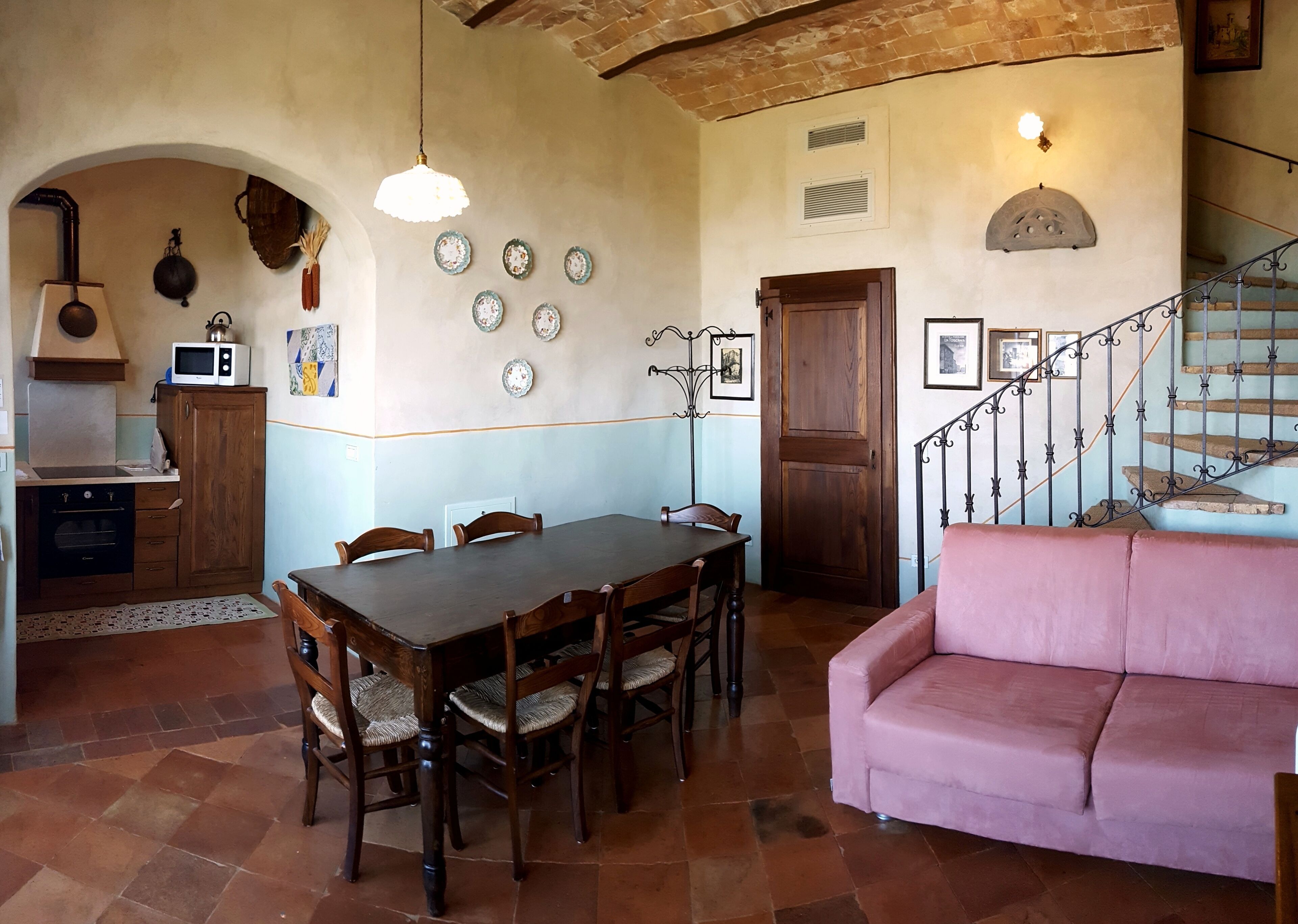 A dining area with a wooden table and chairs, a pink sofa, and a staircase with a wrought iron railing.